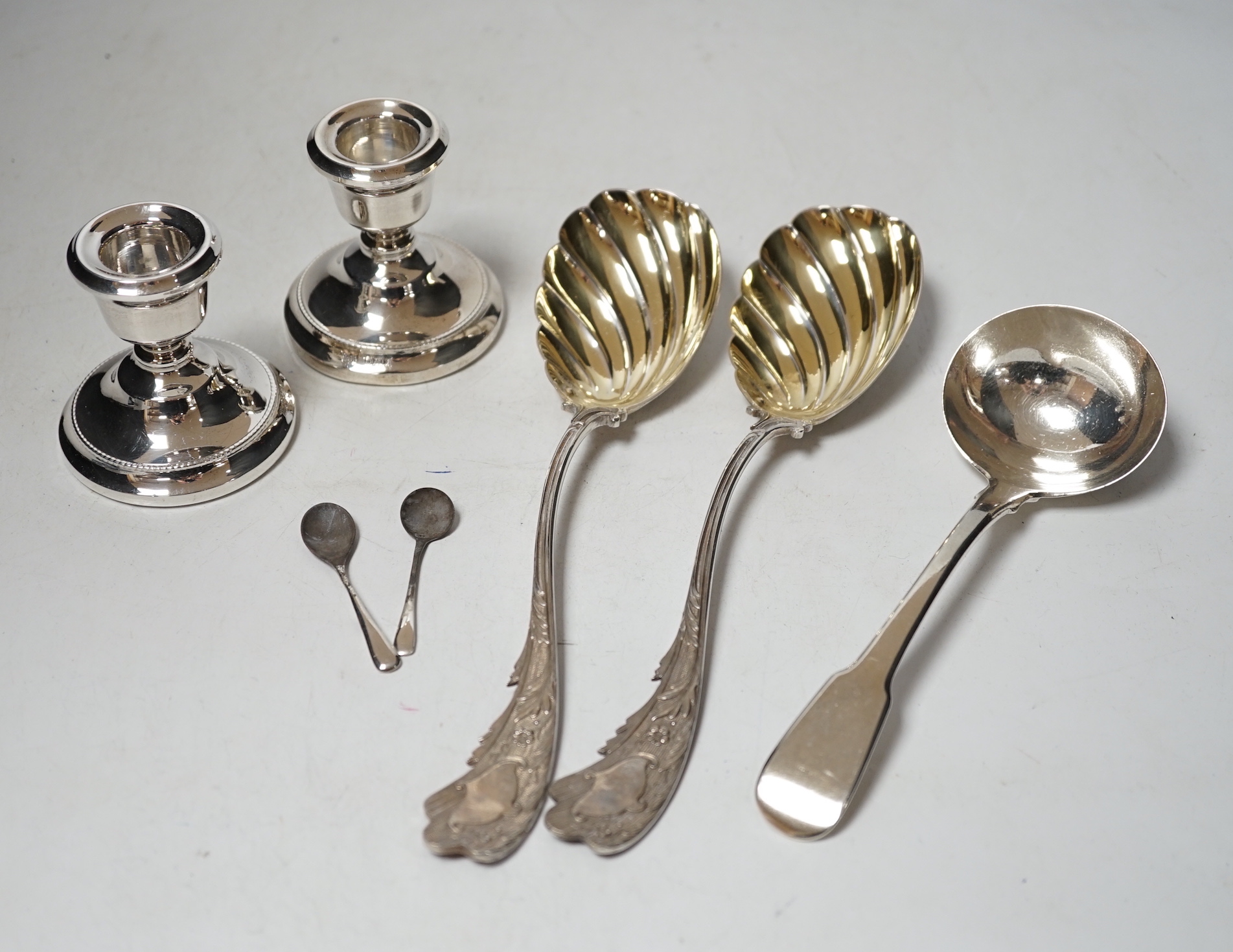 A pair of late Victorian silver serving spoons, with wavy foliate handles, Sheffield, 1897, 22.7cm, three other silver spoons and a pair of silver mounted dwarf candlesticks.